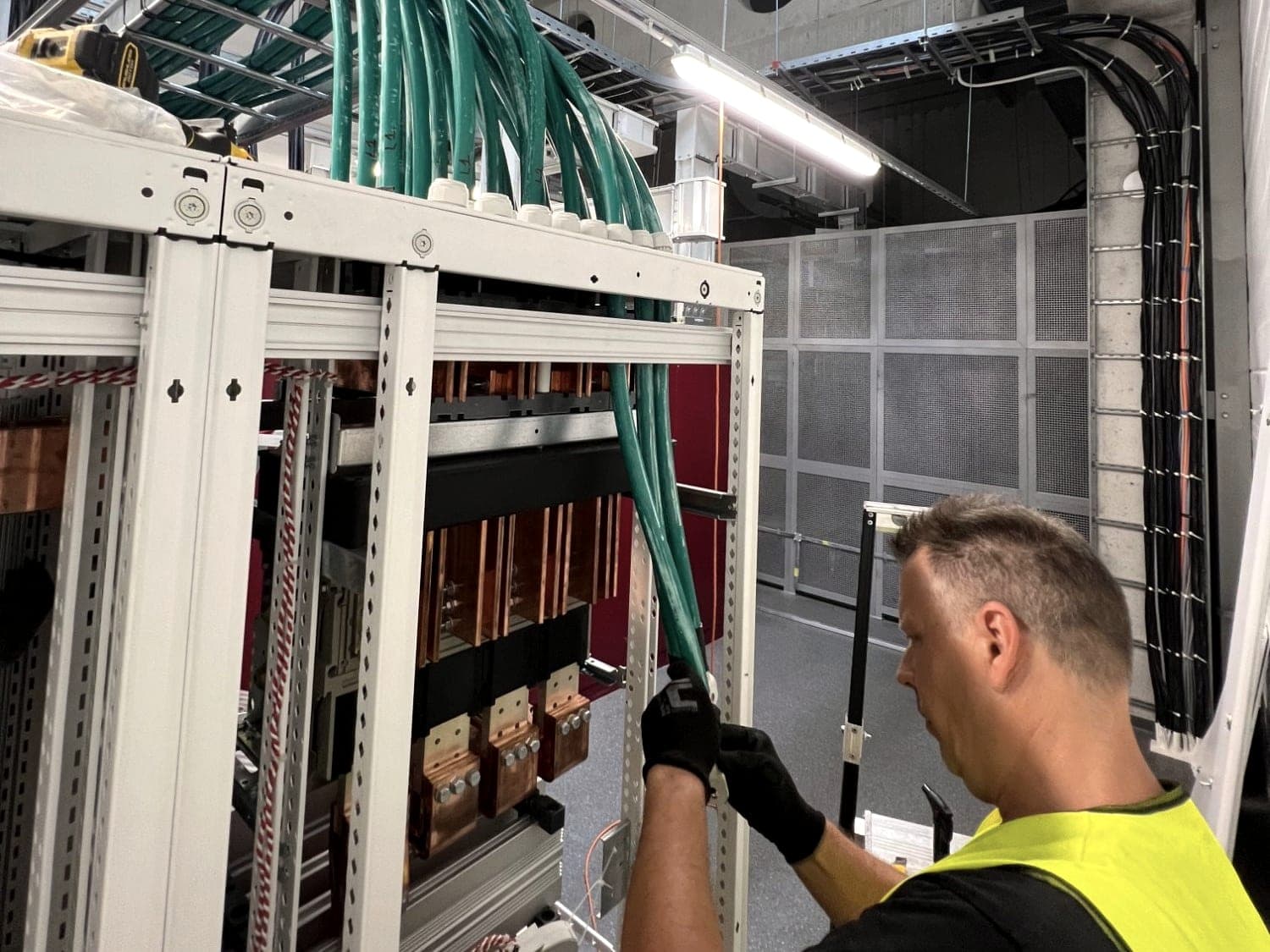 Elektrikář zapojuje silové kabely do hlavního rozváděče NN s měděnými přípojnicemi